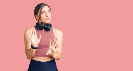 Beautiful caucasian young woman wearing gym clothes and using headphones moving away hands palms...