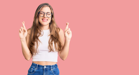 Fototapeta na wymiar Beautiful caucasian young woman wearing casual clothes and glasses gesturing finger crossed smiling with hope and eyes closed. luck and superstitious concept.