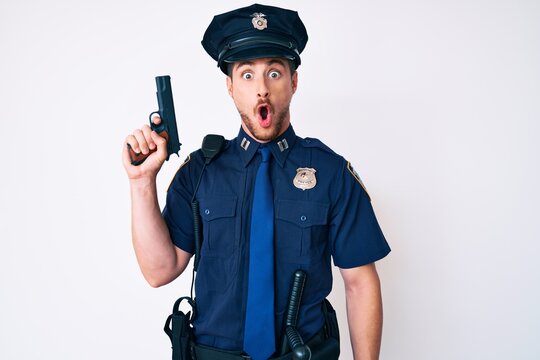 Young caucasian man wearing police uniform holding gun scared and amazed with open mouth for surprise, disbelief face