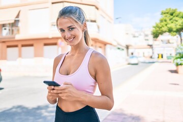 Young blonde sporty girl smiling happy using smartphone at street of city.