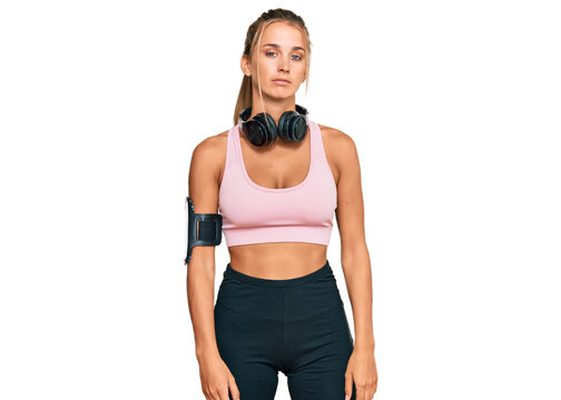 Young blonde woman wearing gym clothes and using headphones relaxed with serious expression on face. simple and natural looking at the camera.