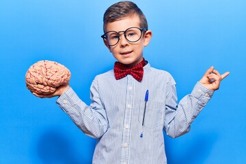 Cute blond kid wearing nerd bow tie and glasses holding brain smiling happy pointing with hand and...