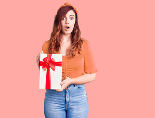 Young beautiful woman holding gift scared and amazed with open mouth for surprise, disbelief face