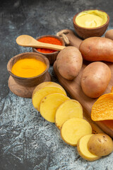 Vertical view of homemade delicious potato chips on wooden cutting board different spices and flavors on newspaper on gray table