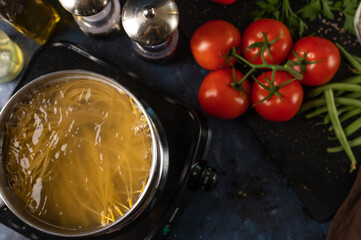 view from above of spaghetti cooking process on marble dark blue table with variety of ingredients background. Backstage of cooking pasta. Close-up view. Cookbook design.