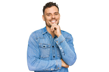 Young hispanic man wearing casual denim jacket looking confident at the camera with smile with crossed arms and hand raised on chin. thinking positive.