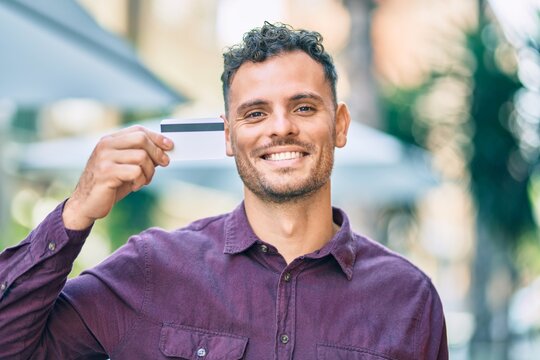 Young hispanic man smiling happy holding credit card at the city.
