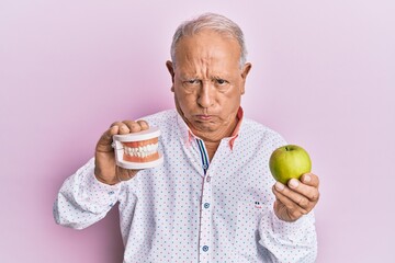 Senior caucasian man holding denture and green apple depressed and worry for distress, crying angry...