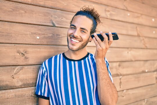 Young hispanic man smiling happy listening smartphone audio message leaning on the wall.