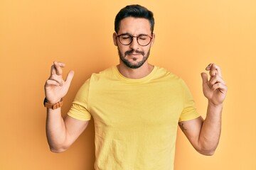 Fototapeta premium Young hispanic man wearing casual clothes and glasses gesturing finger crossed smiling with hope and eyes closed. luck and superstitious concept.