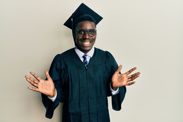 Handsome black man wearing graduation cap and ceremony robe celebrating crazy and amazed for success with arms raised and open eyes screaming excited. winner concept