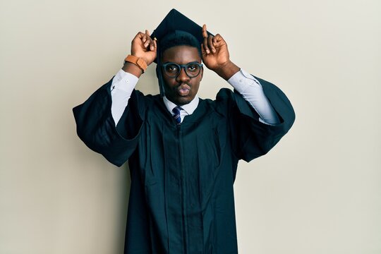 Handsome black man wearing graduation cap and ceremony robe doing funny gesture with finger over head as bull horns