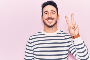 Young hispanic man wearing casual clothes smiling with happy face winking at the camera doing victory sign. number two.