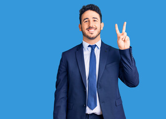 Young hispanic man wearing business clothes smiling with happy face winking at the camera doing victory sign. number two.
