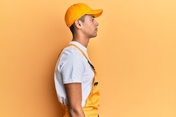 Young handsome african american man wearing handyman uniform over yellow background looking to side, relax profile pose with natural face and confident smile.