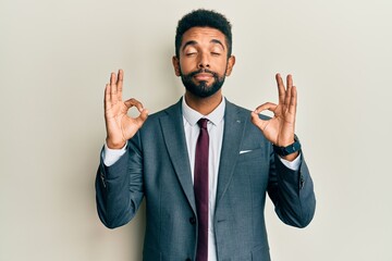 Handsome hispanic man with beard wearing business suit and tie relaxed and smiling with eyes closed doing meditation gesture with fingers. yoga concept.