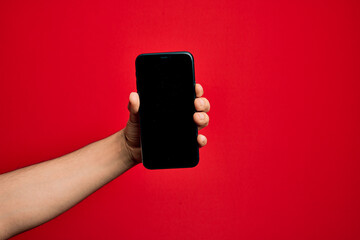 Fototapeta na wymiar Hand of caucasian young man holding smartphone showing screen over isolated red background