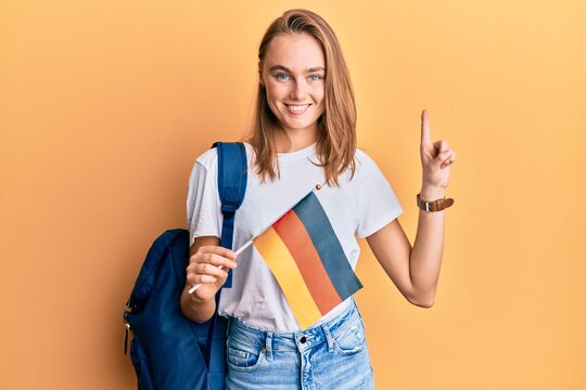 Beautiful blonde woman exchange student holding germany flag smiling with an idea or question pointing finger with happy face, number one