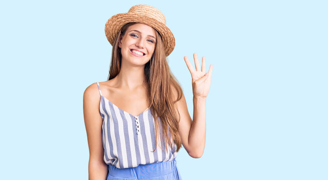 Young beautiful blonde woman wearing summer hat showing and pointing up with fingers number four while smiling confident and happy.