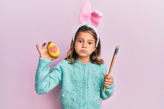 Little beautiful girl wearing cute easter bunny ears holding colored egg puffing cheeks with funny face. mouth inflated with air, catching air.