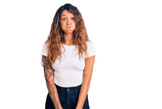 Young hispanic woman with tattoo wearing casual white tshirt puffing cheeks with funny face. mouth inflated with air, crazy expression.