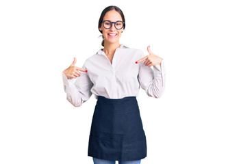 Beautiful brunette young woman wearing professional waitress apron looking confident with smile on face, pointing oneself with fingers proud and happy.