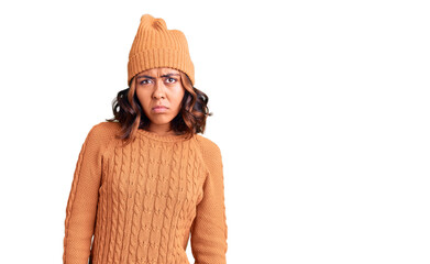 Young beautiful mixed race woman wearing wool sweater and winter hat skeptic and nervous, frowning...