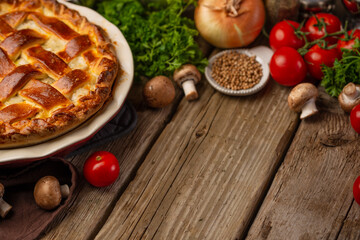 Ruddy pie with mushrooms and chicken on wooden table with variety of ingredients background. Concept of cooking process. Backstage of preparing tasty meal. Side view. Recipe book. Space for text.