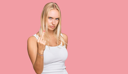 Young blonde girl wearing casual style with sleeveless shirt showing middle finger, impolite and...
