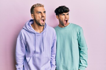 Homosexual gay couple standing together wearing casual clothes angry and mad screaming frustrated and furious, shouting with anger. rage and aggressive concept.