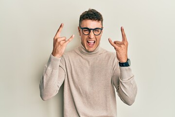 Fototapeta premium Hispanic young man wearing casual turtleneck sweater shouting with crazy expression doing rock symbol with hands up. music star. heavy music concept.