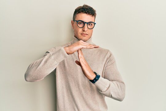 Hispanic young man wearing casual turtleneck sweater doing time out gesture with hands, frustrated and serious face