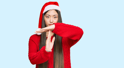 Young chinese woman wearing christmas hat doing time out gesture with hands, frustrated and serious...