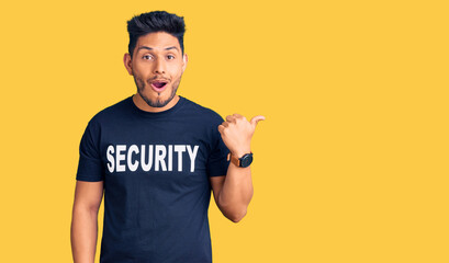 Handsome latin american young man wearing security t shirt surprised pointing with finger to the...