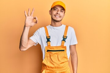 Hispanic young man wearing handyman uniform smiling positive doing ok sign with hand and fingers. successful expression.