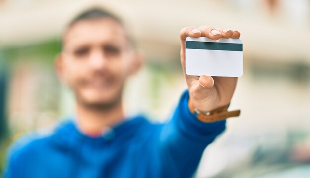 Young hispanic man smiling happy holding credit card at the city