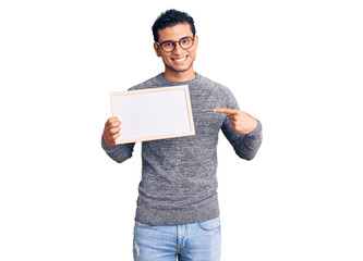 Hispanic handsome young man holding blank empty banner smiling happy pointing with hand and finger