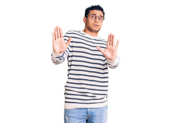 Naklejka premium Hispanic handsome young man wearing casual clothes and glasses afraid and terrified with fear expression stop gesture with hands, shouting in shock. panic concept.