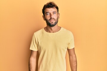 Handsome man with beard wearing casual yellow tshirt over yellow background relaxed with serious expression on face. simple and natural looking at the camera.