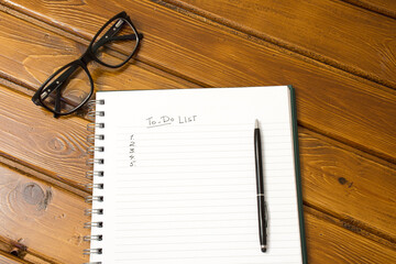 "Wish list" is written on notepad with pen, glasses and calendar on wooden table.