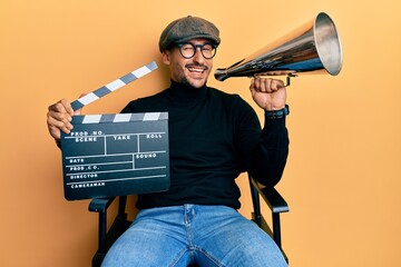 Handsome man with tattoos holding video film clapboard and louder winking looking at the camera...