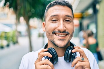 Young hispanic man smiling happy listening to music using headphones at street of city.