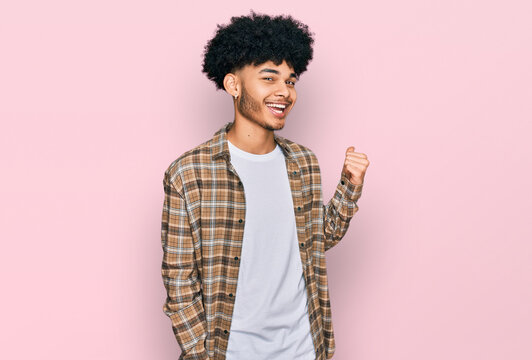Young african american man with afro hair wearing casual clothes smiling with happy face looking and pointing to the side with thumb up.