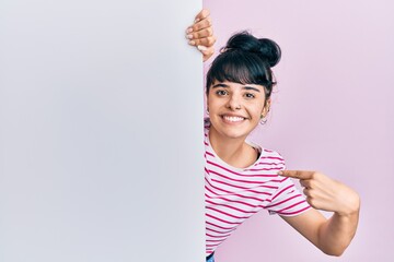 Young hispanic girl holding blank empty banner pointing finger to one self smiling happy and proud