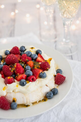 Pavlova with strawberries, raspberries, blueberries and passionfruit and sparkling wine in the foreground