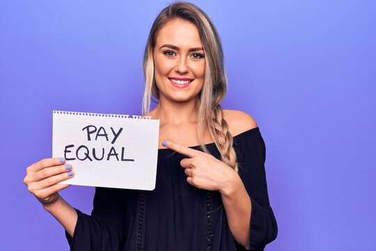 Beautiful blonde woman asking for equality economy holding paper with pay equal message smiling happy pointing with hand and finger
