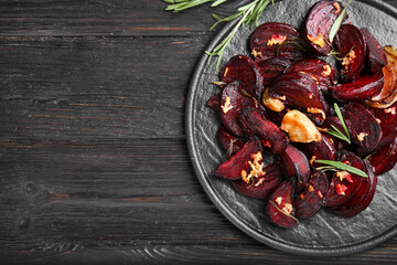 Roasted beetroot slices, garlic and rosemary on black wooden table, top view. Space for text