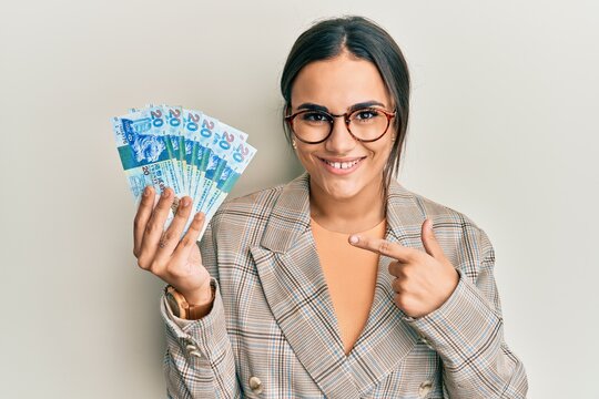Young brunette woman holding hong kong 20 dollars banknotes smiling happy pointing with hand and finger