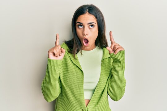 Young brunette woman wearing casual clothes amazed and surprised looking up and pointing with fingers and raised arms.