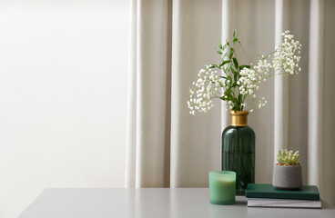 Vase with beautiful flowers, candle and books on grey table indoors, space for text. Interior elements